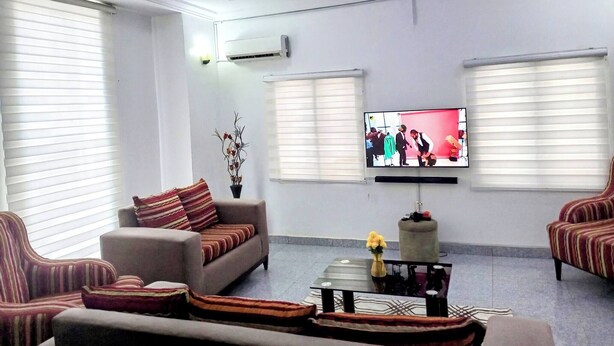A living room with a sofa, armchairs, a coffee table, and a TV. - Lovely 2-bedroom Serviced Apartment With a Balcony (Abuja)