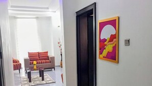 A hallway leading to a living area with a sofa, a coffee table, and a painting on the wall. - Lovely 2-bedroom Serviced Apartment With a Balcony (Abuja)