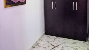 A room with a dark wardrobe, a framed picture on the wall, and a tiled floor. - Lovely 2-bedroom Serviced Apartment With a Balcony (Abuja)