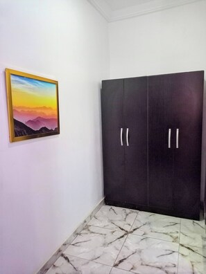 A room with a dark wardrobe, a framed picture on the wall, and a tiled floor.