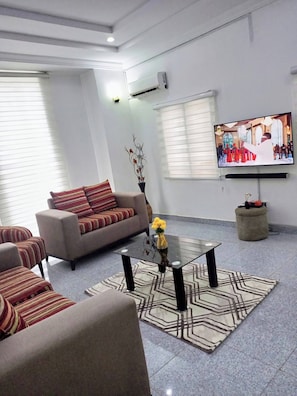 A living room with a sofa, armchairs, a coffee table, a TV, and a decorative vase.