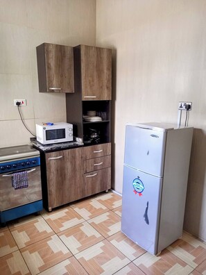 A compact kitchen with a microwave, stove, wooden cabinets, and a refrigerator.