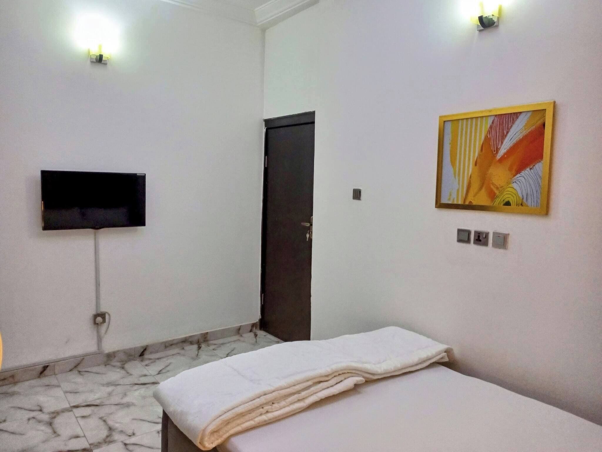 Une chambre d’hôtel avec un lit, un téléviseur à écran plat fixé au mur, une porte et un tableau.