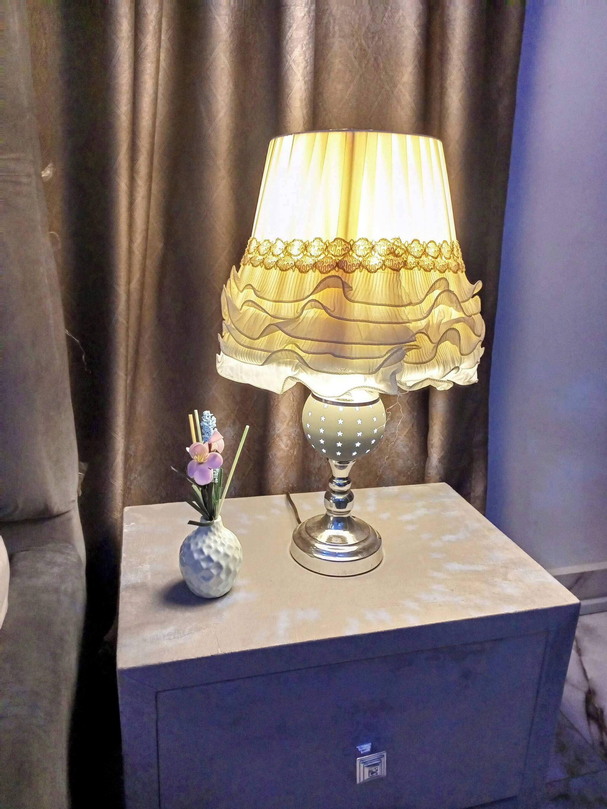 Une table de chevet avec une lampe et un vase de fleurs.