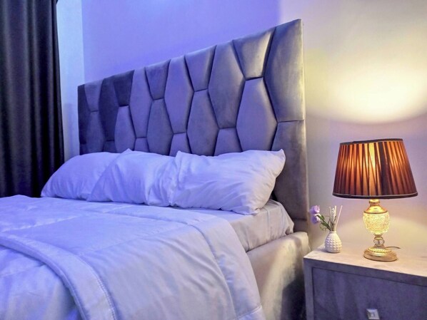 A bed with a tufted headboard, white bedding, and a bedside table with a lamp and a vase.