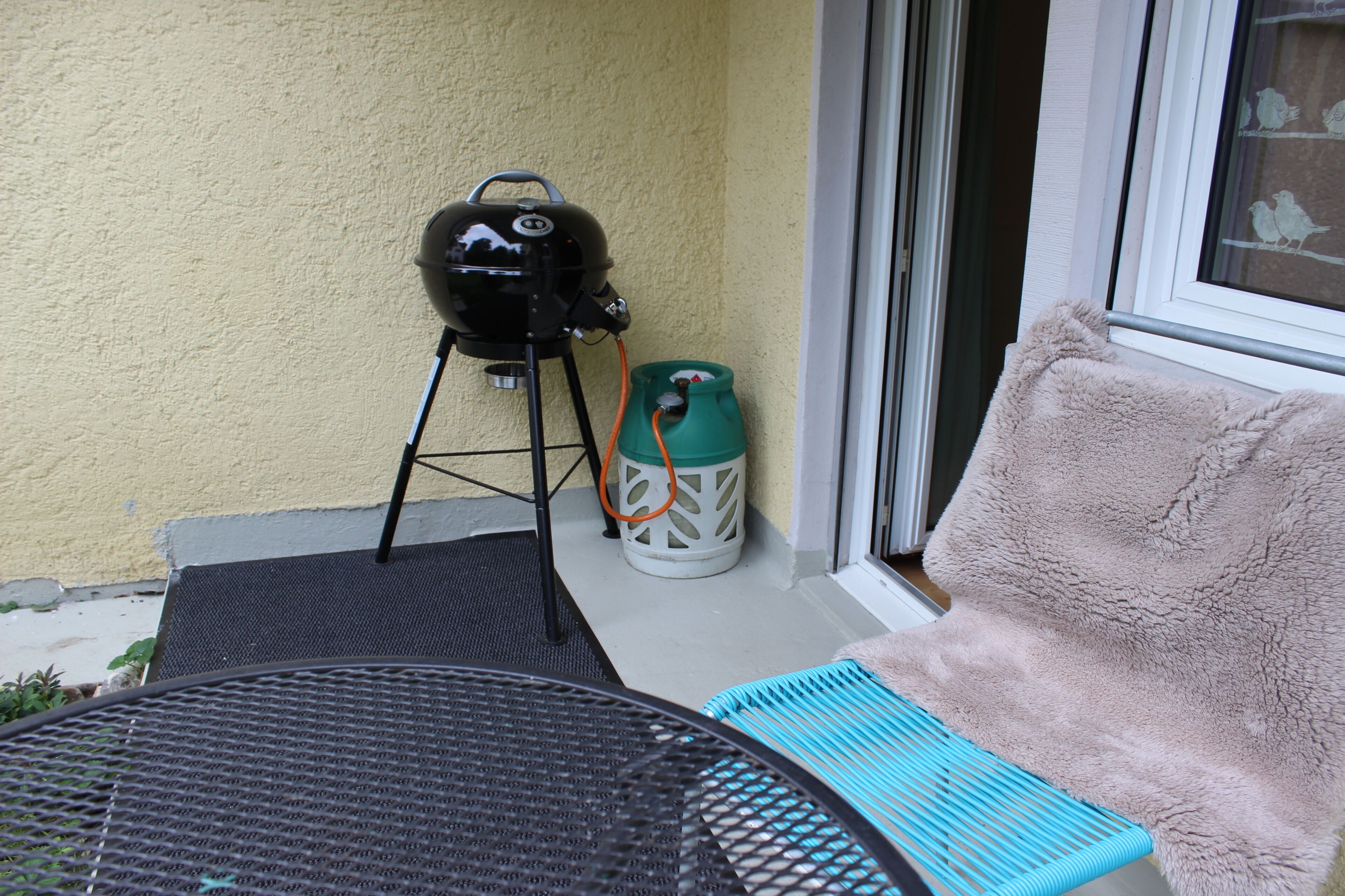 A patio with a grill, a blue cushioned chair, and a fluffy beige chair.