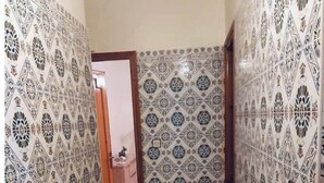 Um corredor com paredes e piso de azulejos estampados, que leva a um quarto com porta.