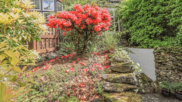 A stone building with a garden featuring red flowers and a wooden fence.