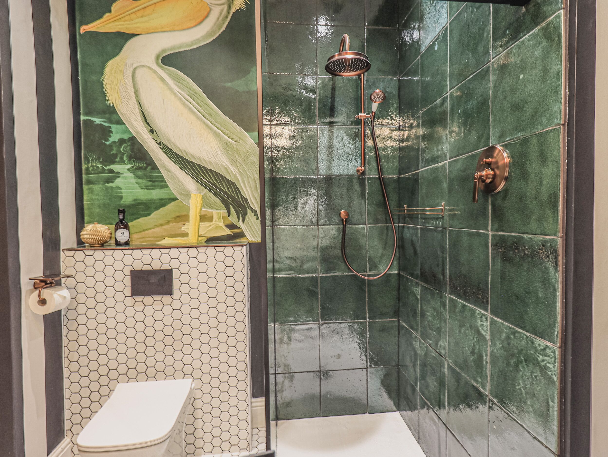 Un baño con inodoro, ducha con cabezal de lluvia y un mural de un pájaro.
