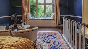 A room with a bay window, a dining area with a table and chairs, a potted plant, and a patterned rug.