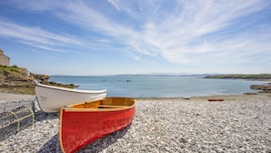 Uma praia de pedras com dois barcos, um branco e um vermelho, e um litoral rochoso.