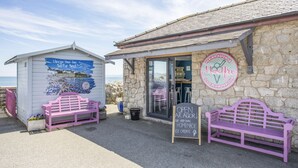 Uma gelataria à beira-mar com paredes de pedra, dois bancos cor-de-rosa e uma placa anunciando sorvetes artesanais.