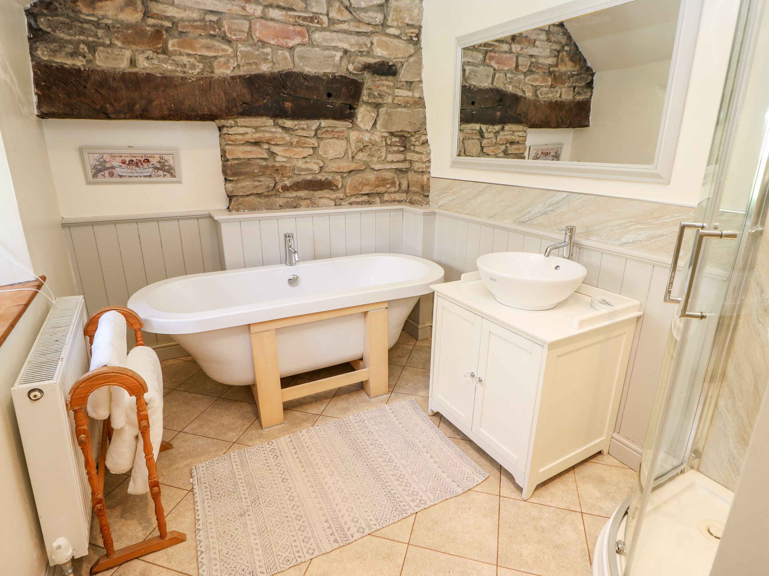 A bathroom with a stone wall, a freestanding bathtub, a sink, and a mirror.