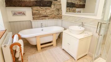 A bathroom with a stone wall, a freestanding bathtub, a sink, and a mirror.