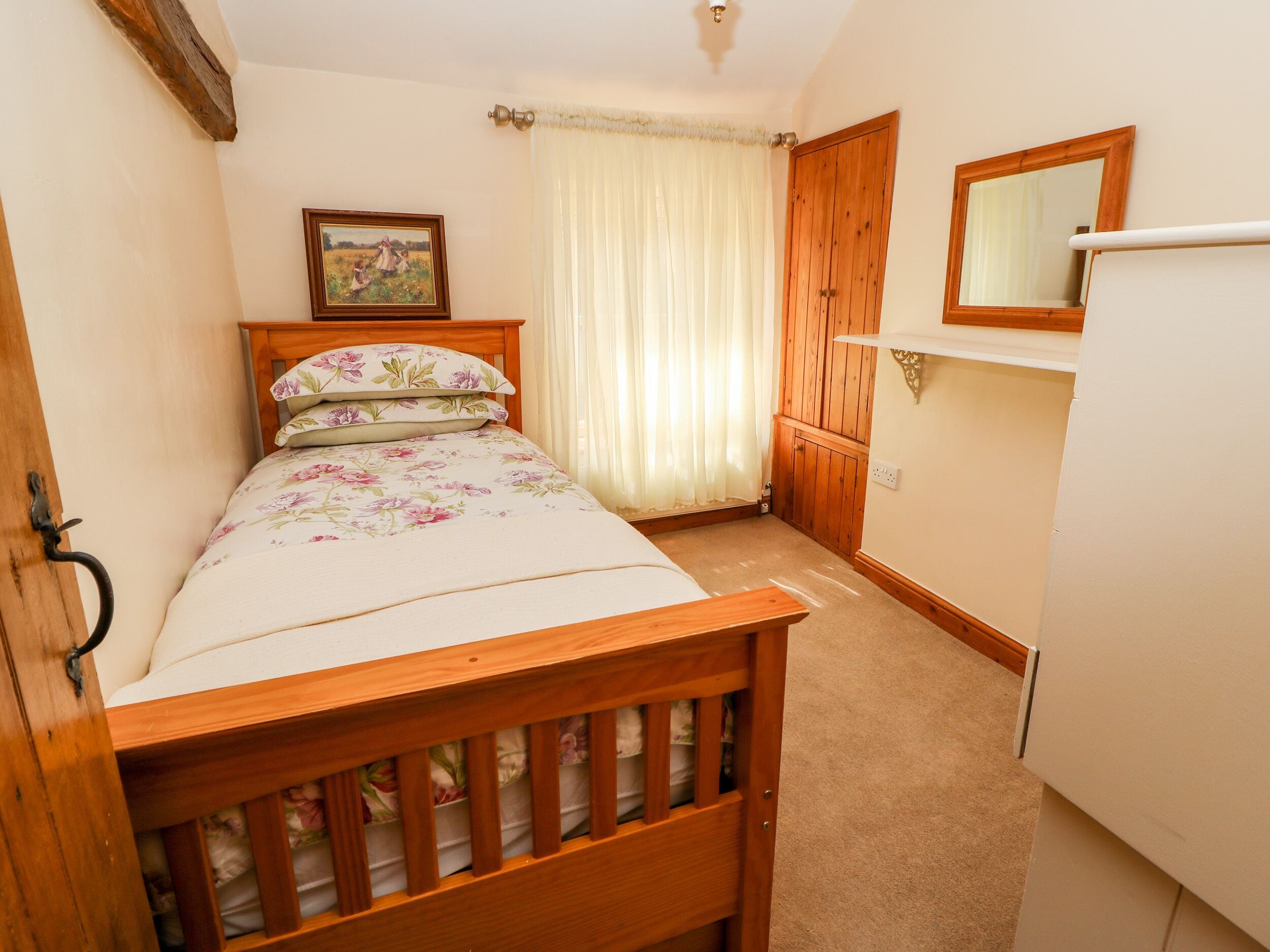 A small, cozy bedroom with a wooden bed, a bedside table, a mirror, and a door leading to another room.