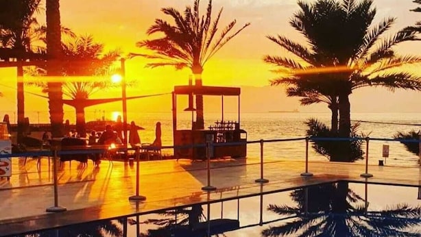 Une terrasse au bord de l’eau, agrémentée de palmiers, d’un belvédère et offrant une vue dégagée sur le coucher de soleil sur l’eau.