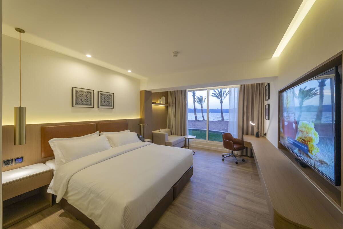 Une chambre d’hôtel moderne dotée d’un grand lit, d’un bureau, d’une chaise, d’une télévision et offrant une vue sur la plage.