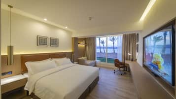 Una habitación de hotel moderna con una cama grande, un escritorio, una silla, un televisor y vista a la playa.