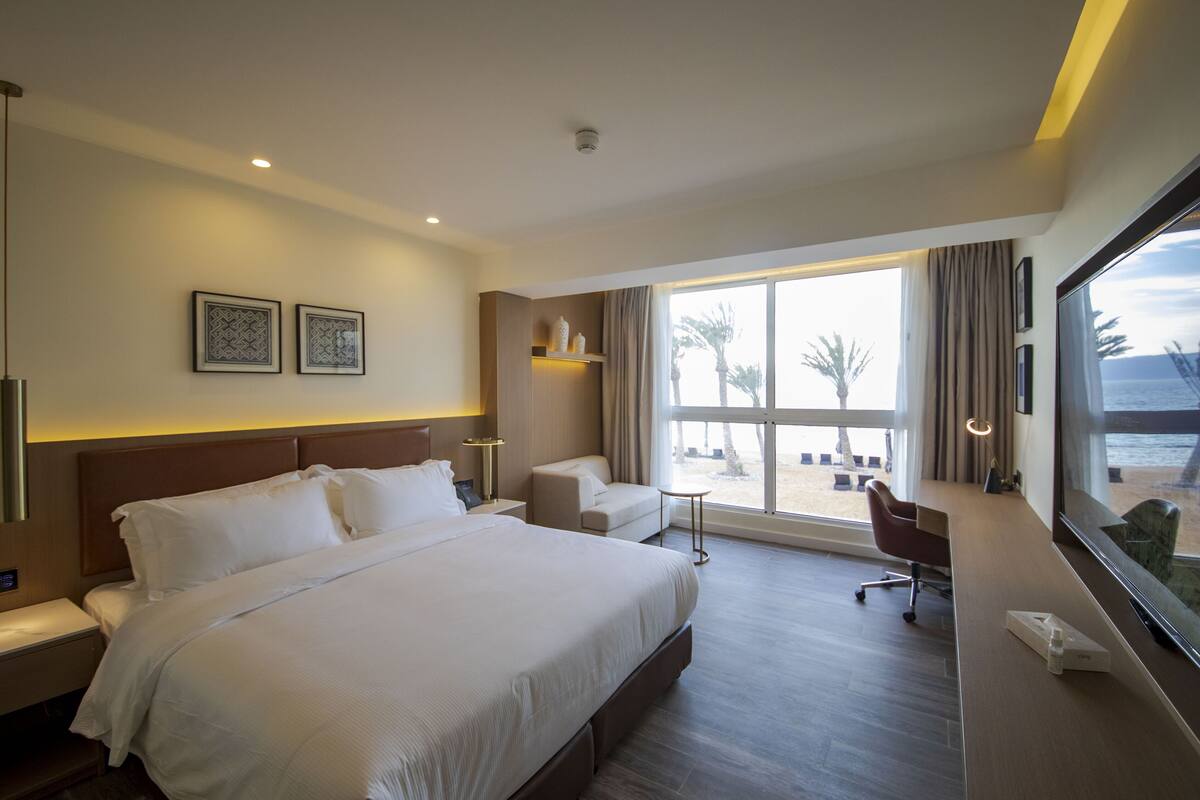 Une chambre d’hôtel avec un grand lit, un bureau, une chaise et une vue sur la plage.