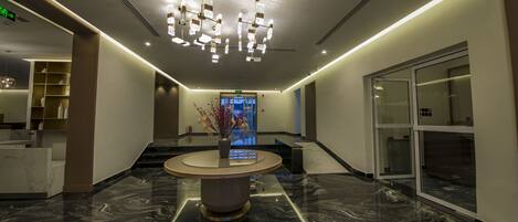 A modern lobby with a marble floor, a central round table, and a chandelier.