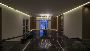 Un hall d’hôtel moderne avec un sol en marbre, un lustre central et une vue sur la mer par une grande fenêtre.