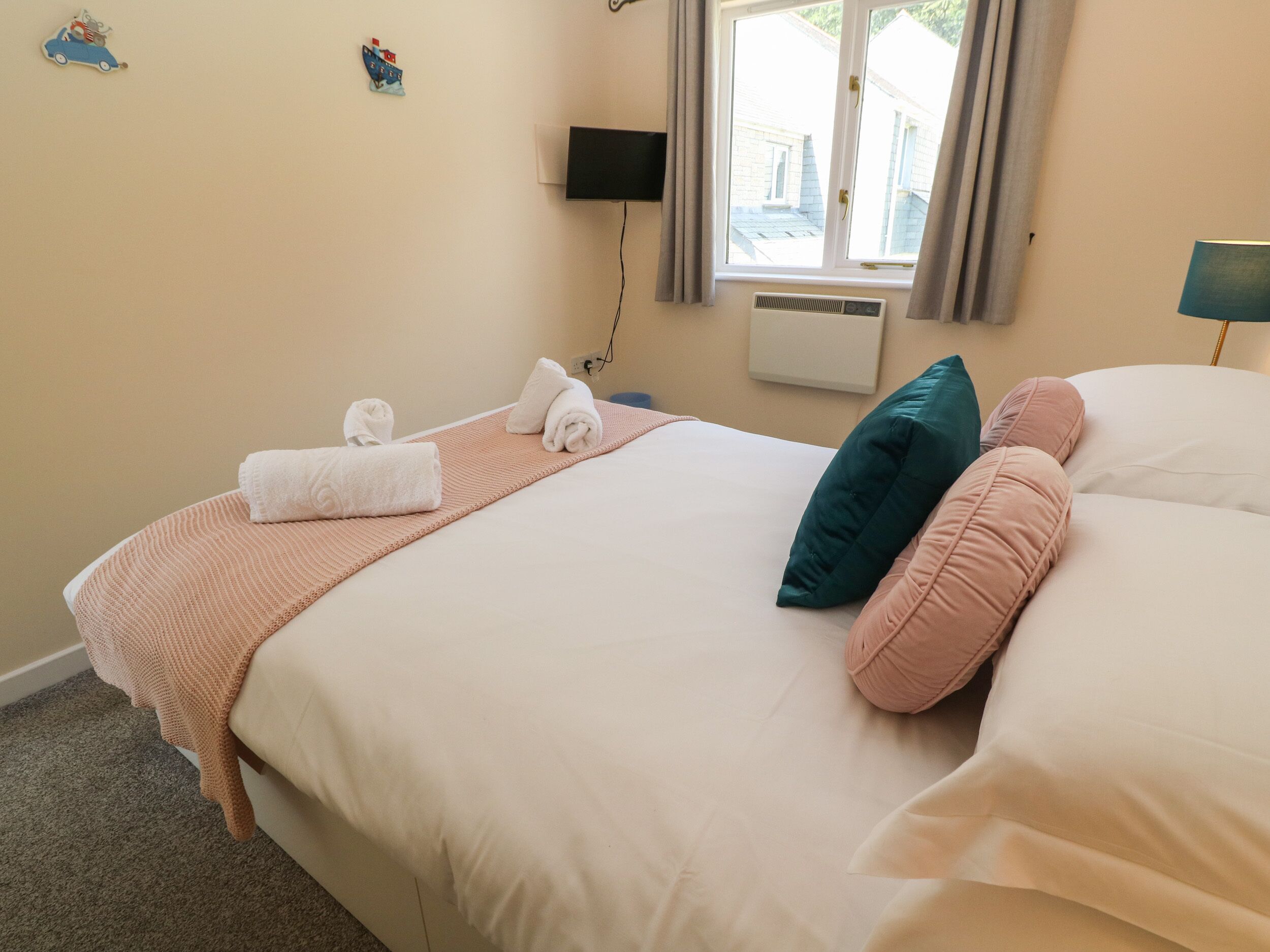 Ein ordentlich gemachtes Bett mit weißen und rosafarbenen Kissen, einer rosafarbenen Decke und zwei aufgerollten Handtüchern.