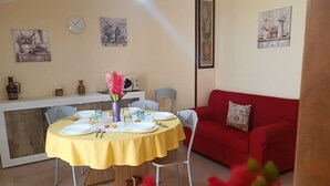 A dining area with a yellow table set for four, a red sofa, and various wall decorations including a clock and framed pictures. - Casa AuroraRosa (Tropea)