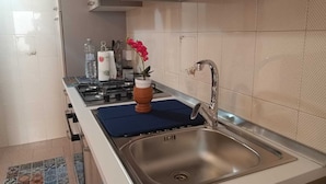 A modern kitchen with a stainless steel sink, a gas stove, and a blue mat on the countertop. - Casa AuroraRosa (Tropea)
