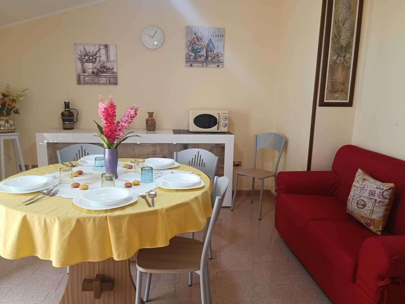 A dining area with a yellow tablecloth, white plates, and a vase of pink flowers.
