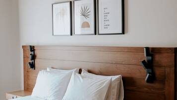 Een netjes opgemaakt bed met witte lakens, een houten hoofdbord en nachtkastjes met zwarte lampen. Boven het bed hangen drie ingekaderde foto's.