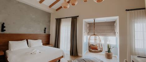 Une chambre spacieuse avec un grand lit, des poutres apparentes, un fauteuil suspendu et une vue par la fenêtre.