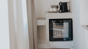 A compact kitchenette with a coffee maker and a mini-fridge, a beige curtain, and a white wall. - Paye Alaçatı (Cesme)