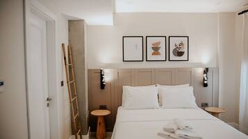 Een hotelkamer met een bed, twee nachtkastjes, een ladder en drie ingelijste foto’s aan de muur.