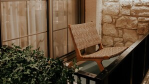A balcony with a wicker chair, a potted plant, and a stone wall. - Paye Alaçatı (Cesme)
