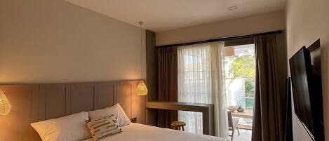 A hotel room with a large bed, a flat-screen TV, a small table, and a view of the outside.