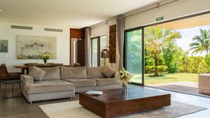 A modern living room with a sectional sofa, a coffee table, and a large window offering a view of a tropical garden. - Villa Paolita  (Vieux Grand Port)