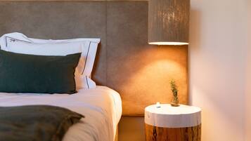 Una cama bien hecha con almohadas, una lámpara de noche y una mesita de madera con un florero.