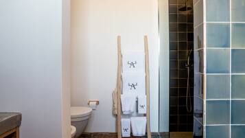Een badkamer met een houten handdoekrek vol witte handdoeken, een toilet en een douchegedeelte met blauwe tegels.