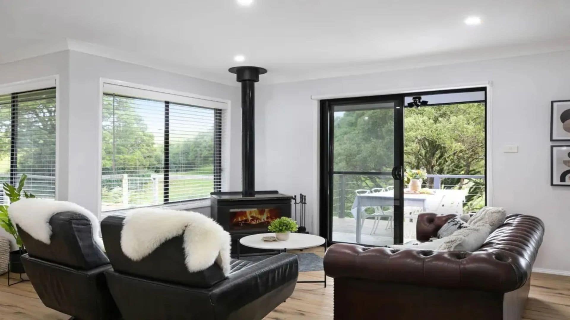 A modern living room with a fireplace, a sofa, a dining table, and a view through a glass door to the outdoors.