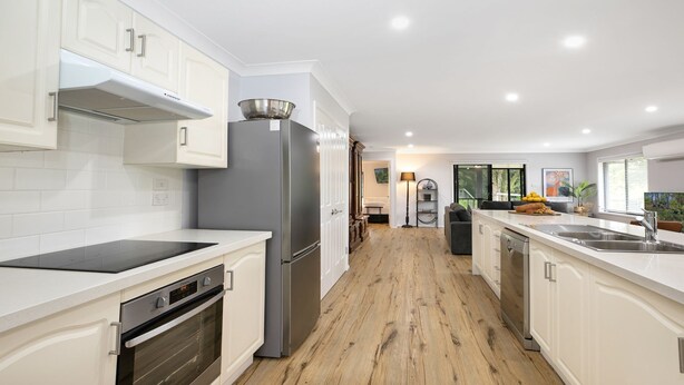 A modern kitchen with white cabinetry, a stainless steel refrigerator, a built-in oven, and a wooden floor.