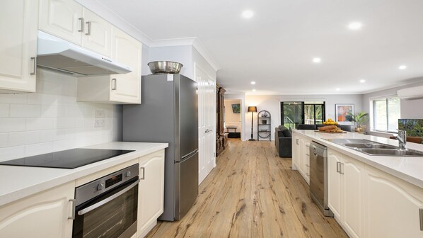 A modern kitchen with white cabinetry, a stainless steel refrigerator, a built-in oven, and a wooden floor.