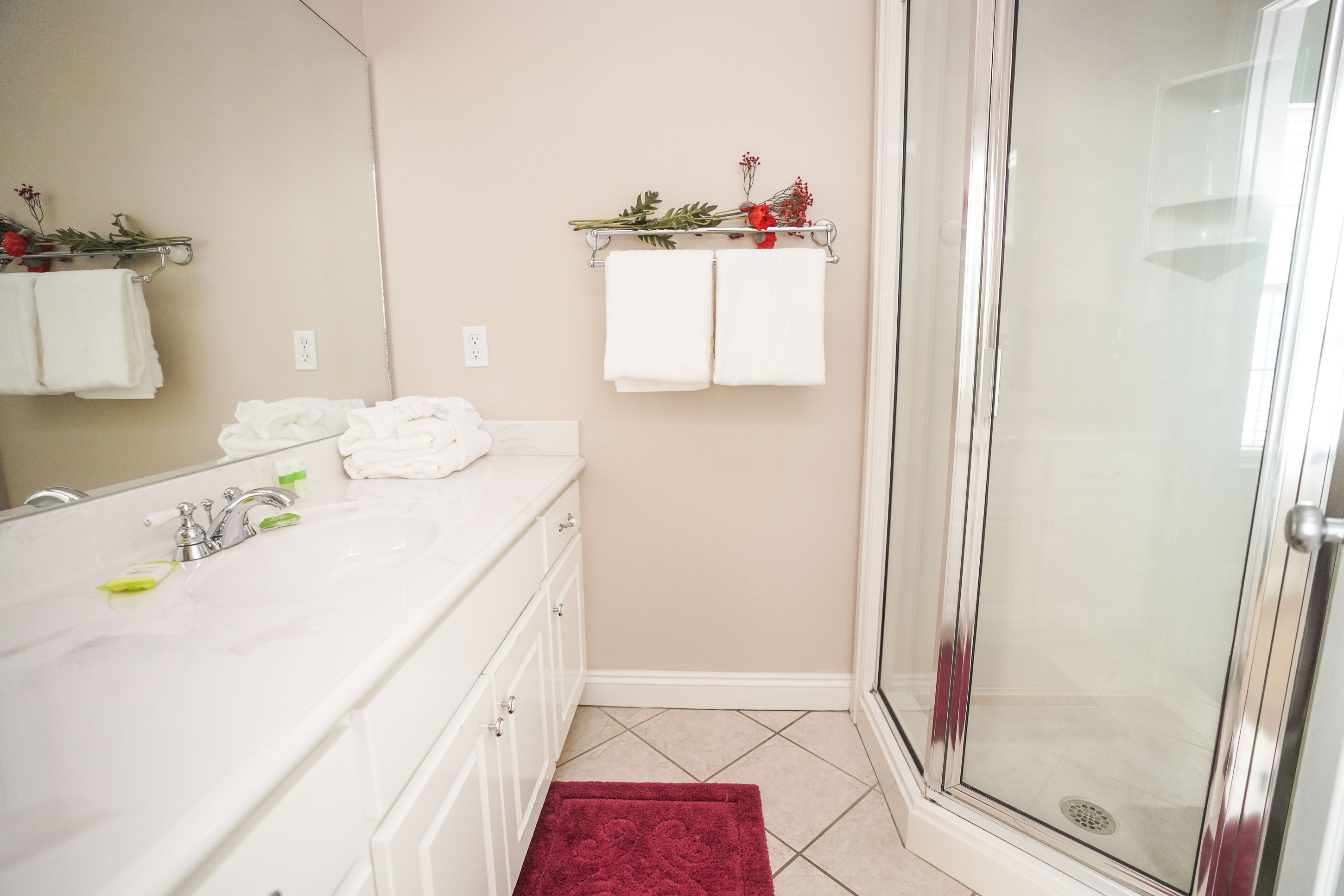 A bathroom with a white vanity, a glass shower enclosure, and a beige wall.