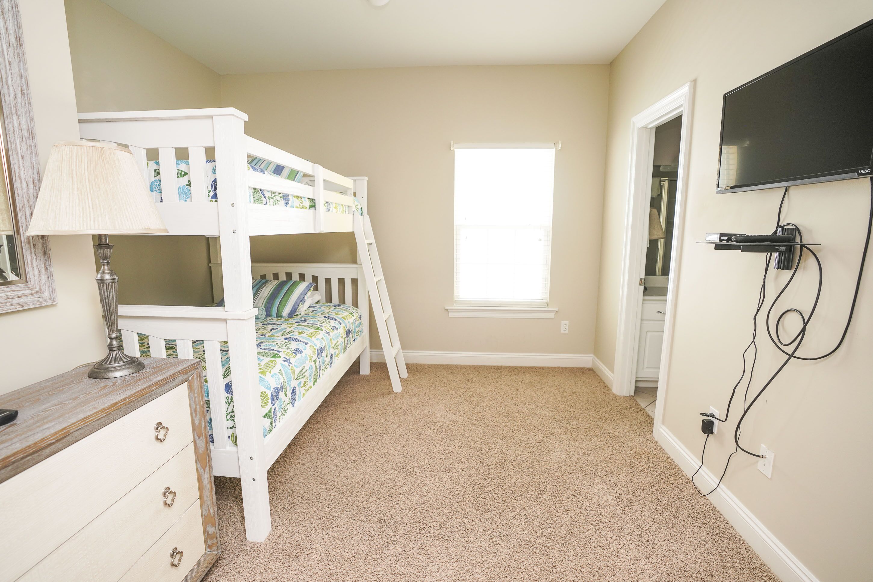A child's bedroom with bunk beds, a dresser, a lamp, a TV, and a window.
