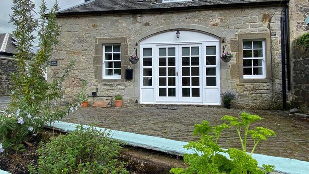 A stone building with a large white door, two windows, and a small dormer window. - Charming Barn Conversion on Private Estate (Kilmarnock)