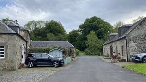 A stone building with a paved driveway and parked cars. - Charming Barn Conversion on Private Estate (Kilmarnock)