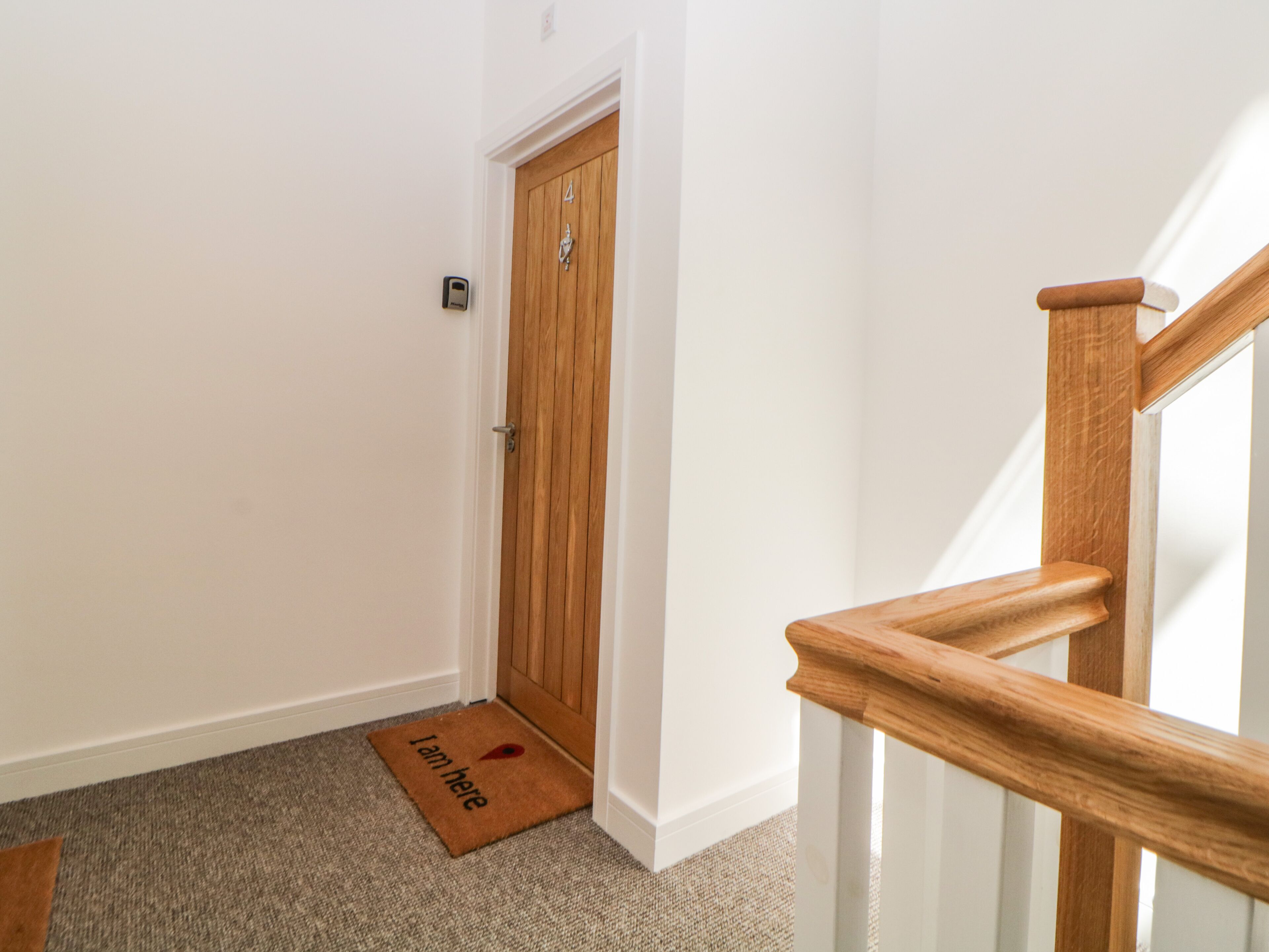 A hallway with a wooden door, a doormat, and a carpeted floor.