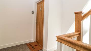 A hallway with a wooden door, a doormat, and a carpeted floor.