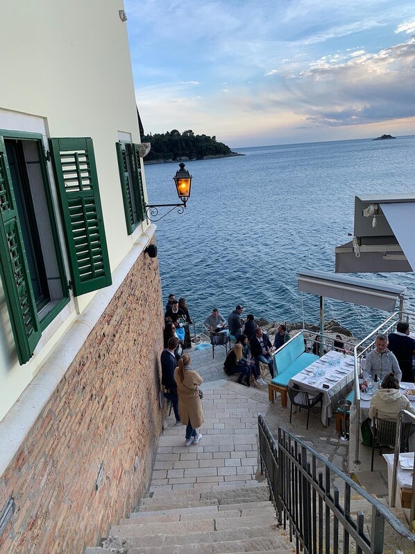 Eine Küstenstraße mit einer Steintreppe, die zu einer Terrasse mit Blick aufs Meer führt.