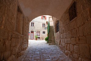 Ein schmaler Kopfsteinpflastergang mit Steinmauern, einer Holztreppe und einer kleinen Außenbestuhlung mit Stühlen und einem Tisch.