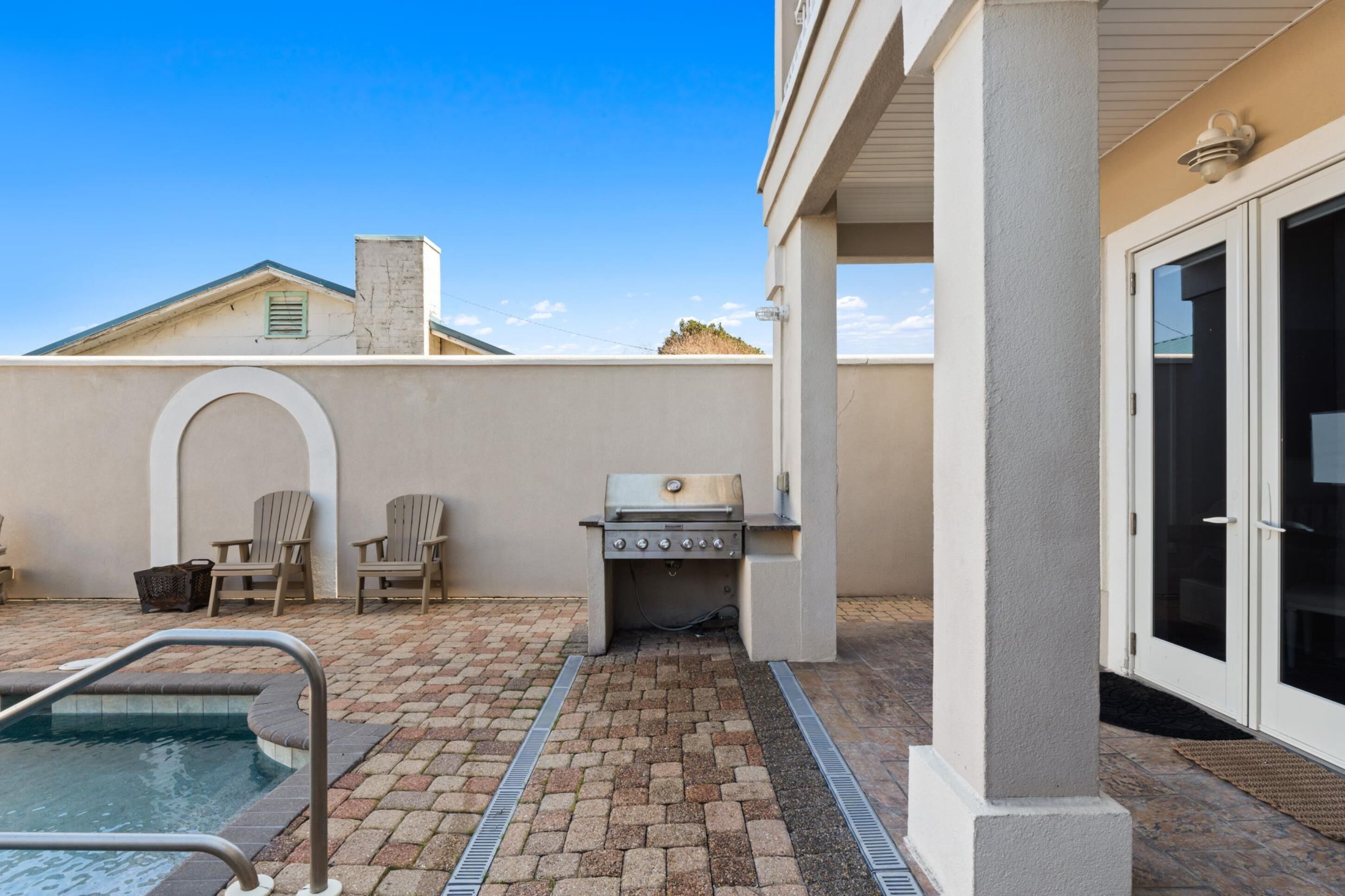 Zona de piscina con una parrilla, sillas y una puerta.
